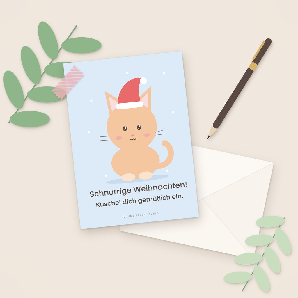 Weihnachtskarte Katze mit Weihnachtsmütze auf dem Schreibtisch mit Stift