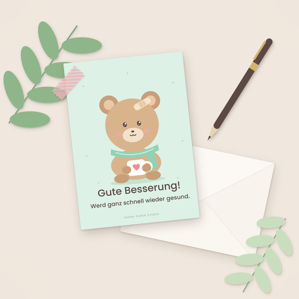 Gute-Besserung-Karte Bär mit Pflaster auf dem Schreibtisch mit Stift
